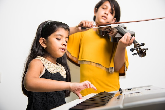 Crianças e conceito de música - garotinhas indianas tocando instrumentos musicais como piano, teclado ou violino