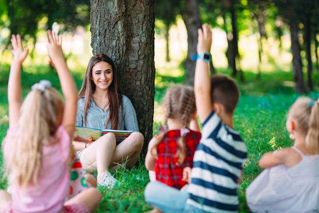 Crianças e educação, jovem no trabalho como livro de leitura do educador para meninos e meninas no parque.