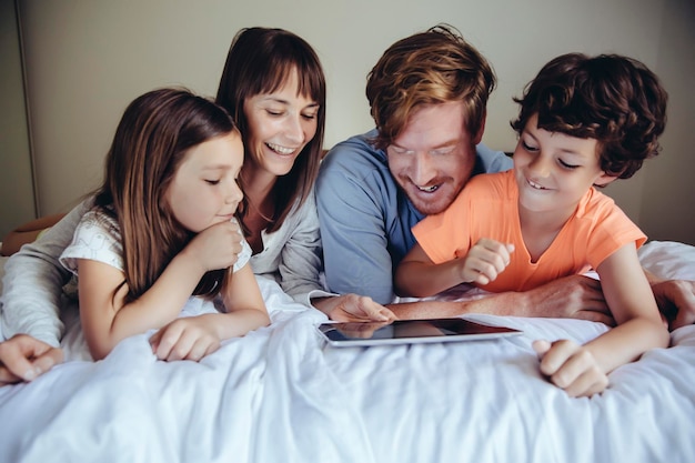Crianças e seus pais olhando para tablet na cama