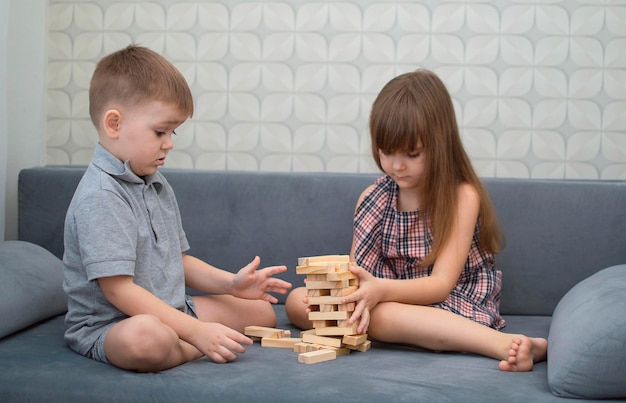 Crianças em casa no sofá jogando torre de remoção de bloco de madeira do jogo. menina e menino se divertem juntos. jogo de tabuleiro e conceito para entretenimento infantil.