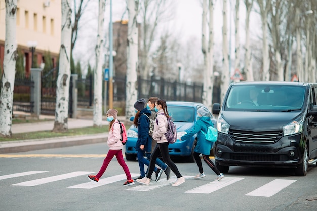 Crianças em idade escolar atravessam a rua com máscaras médicas. As crianças vão para a escola.