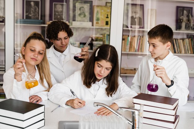 Crianças em idade escolar estudando na aula de química em sala de aula Alunos escrevendo em caderno segurando frascos com líquido para experimentos e se divertindo juntos Educação escolar