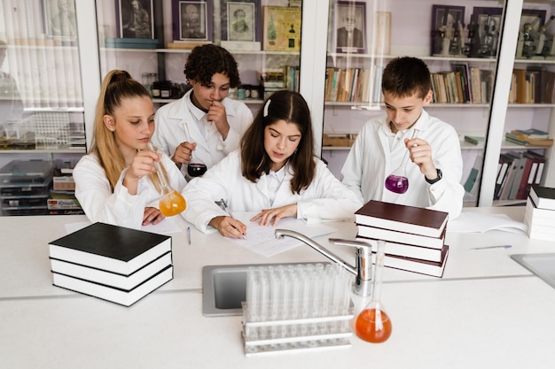 Crianças em idade escolar estudando na aula de química em sala de aula Alunos escrevendo em caderno segurando frascos com líquido para experimentos e se divertindo juntos Educação escolar