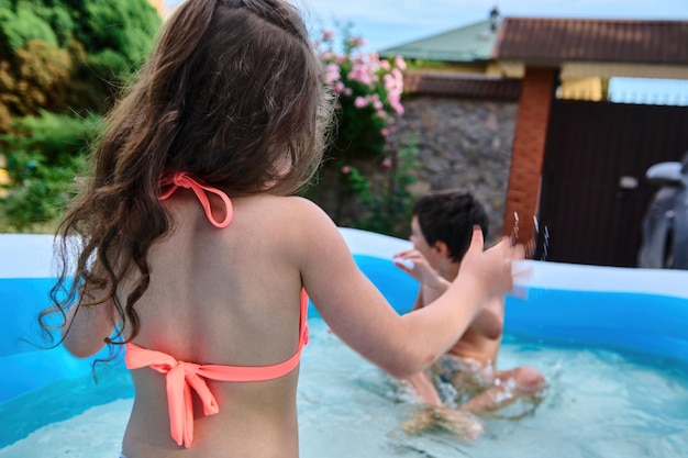 Crianças em idade escolar felizes espirrando água na piscina inflável durante as férias de verão