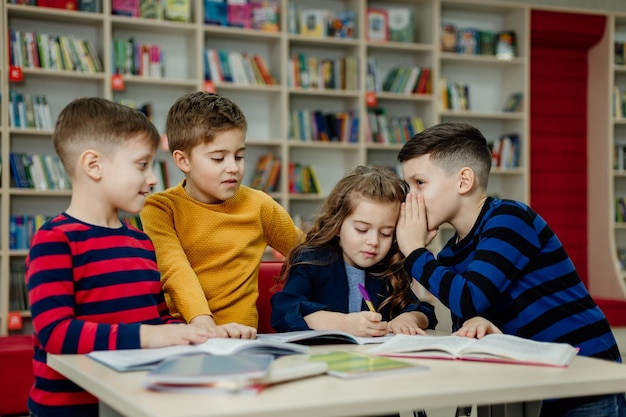 Crianças em idade escolar na biblioteca lendo livros, fazendo lição de casa, preparam um projeto escolar para aulas