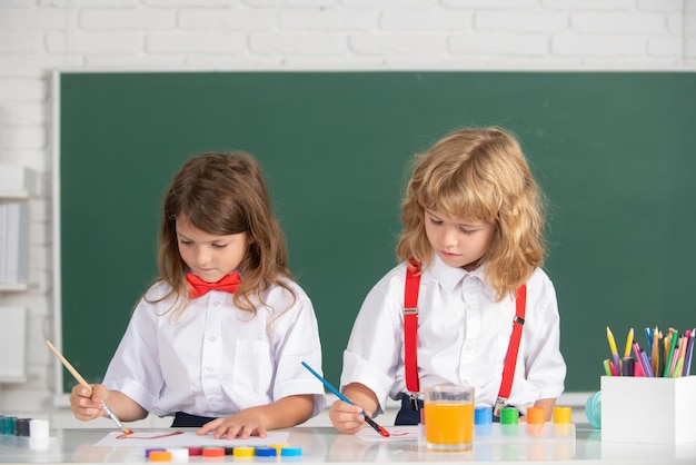 Crianças em idade escolar pintando com tintas de cor e pincel em sala de aula