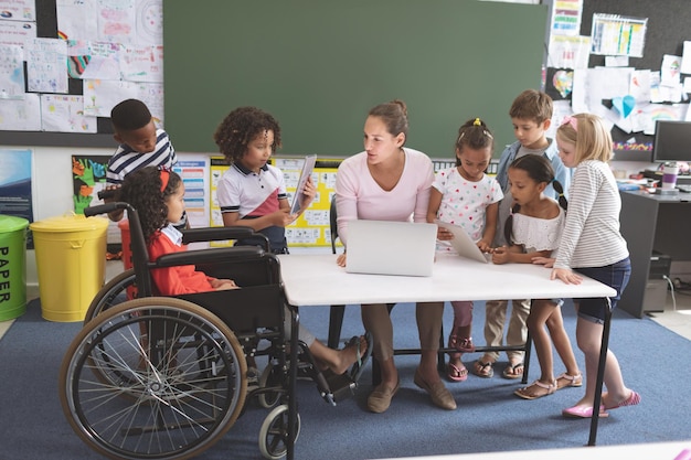 Foto crianças em idade escolar usando tablet digital enquanto o professor interage com os alunos na escola