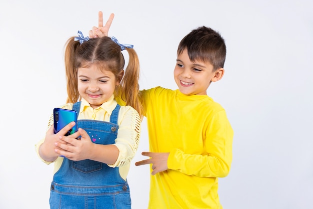 Crianças em idade pré-escolar tiram uma selfie em um smartphone. o menino dá chifres na menina.