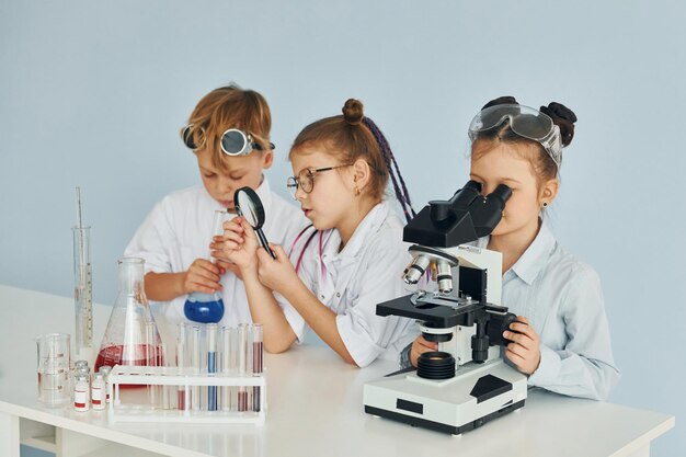 Crianças em jalecos brancos interpretam cientistas em laboratório usando equipamentos