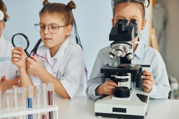 Crianças em jalecos brancos interpretam cientistas em laboratório usando equipamentos