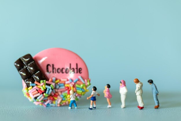 Crianças em miniatura com biscoito de chocolate em pé contra um fundo azul Conceito do Dia Mundial do Chocolate