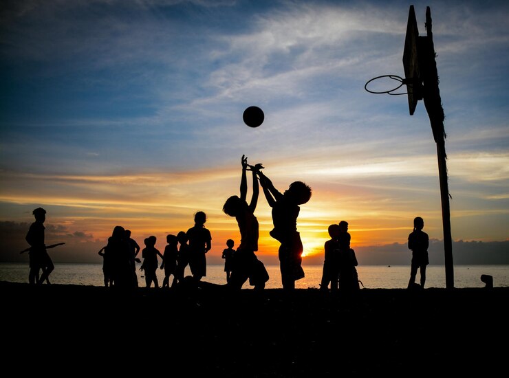 Foto crianças em silhueta jogando basquete na praia contra o céu durante o pôr do sol