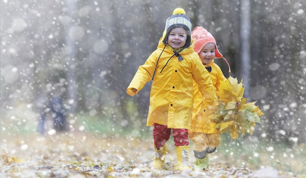 Crianças em uma caminhada no parque outono. Primeira geada e a primeira neve na floresta de outono. As crianças brincam no parque com neve e folhas.