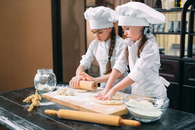 Crianças engraçadas estão preparando a massa na cozinha.