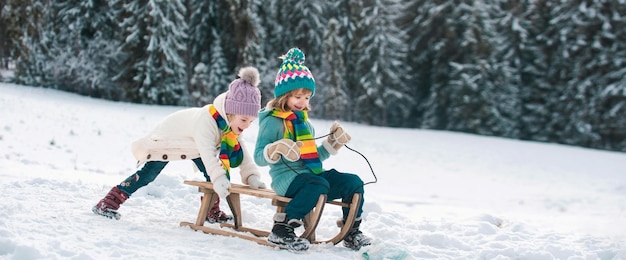 Crianças engraçadas na neve andam de trenó Jogos ao ar livre de inverno Feliz conceito de férias em família de Natal As crianças aproveitam o feriado