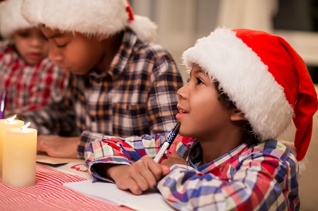 Crianças escrevendo cartas para o Papai Noel. Crianças afro escrevem cartas de Natal. Fazendo uma lista de desejos de Natal. Pense nos melhores presentes.