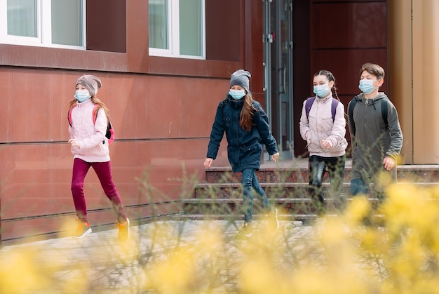 Crianças estudantes com máscaras médicas saem da escola.