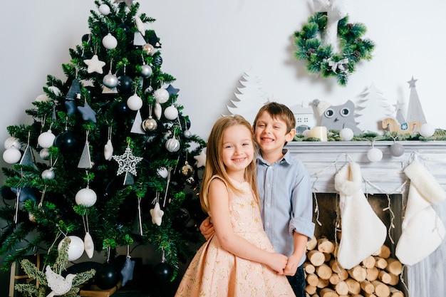 Crianças felizes, abraçando e rindo no estúdio com cristmas árvore e decorações de férias de inverno.