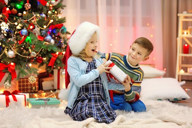 Crianças felizes brincando com presentes na sala decorada de Natal