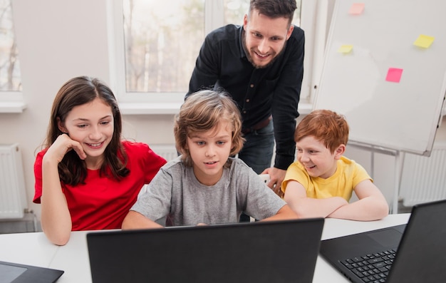 Crianças felizes com a professora realizando tarefas no laptop