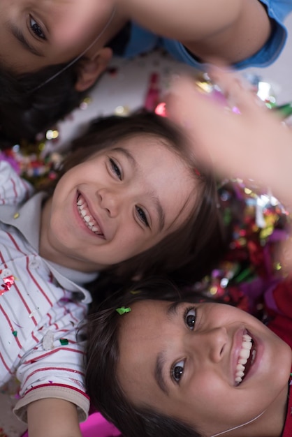Crianças felizes comemorando festa com confete soprando enquanto estava deitado no chão