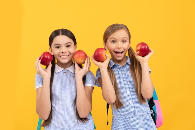 Crianças felizes de volta à escola segurando maçãs para uma alimentação saudável de fundo amarelo, nutrição infantil.