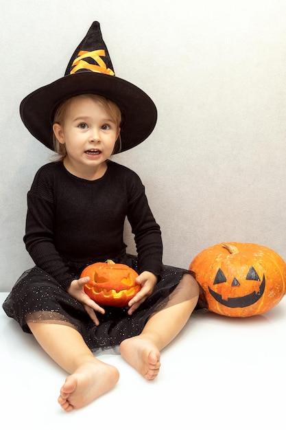 Crianças felizes do Dia das Bruxas enganam ou tratam garotinha com um chapéu de bruxa preto se divertindo com abóbora no interior