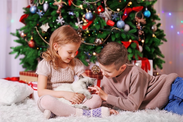 Crianças felizes e gato fofo na sala decorada de Natal