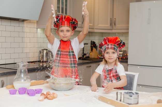 crianças felizes em fantasias de chef preparam massa com farinha, leite, ovos para doces de Natal