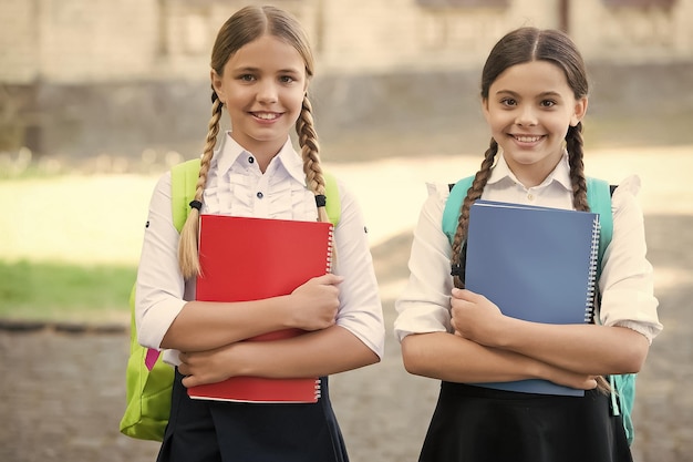 Crianças felizes em uniformes escolares seguram livros de estudo ao ar livre