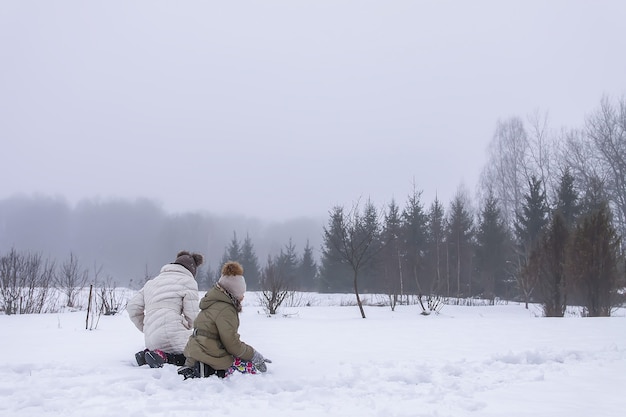 Crianças felizes fazem um boneco de neve em um campo coberto de neve na zona rural.