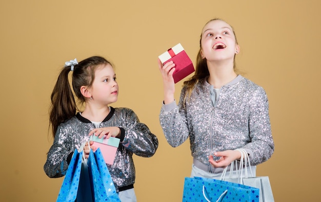 Crianças felizes Irmãzinhas com caixa de presente Compras de férias da irmandade Assistente de loja de moda infantil com pacote Vendas e descontos Meninas pequenas com sacolas de compras Discussão de compras