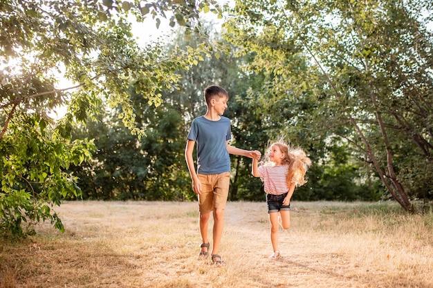 Crianças felizes menino e menina brincam no parque. o irmão mais velho brinca com sua irmã na natureza nos raios do sol de um dia de verão.