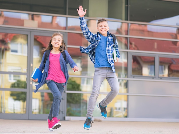 Crianças felizes menino e menina com livros e mochilas no primeiro ou último dia de escola Crianças de escola comemorando o fim do semestre Estudantes para completar o ano acadêmico Retrato ao ar livre de comprimento completo