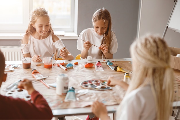 Crianças felizes pintando em papel com tintas coloridas na escola