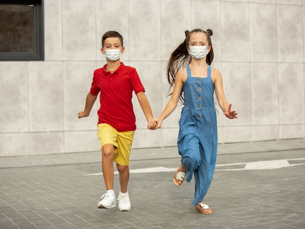 Crianças felizes usando máscara protetora, pulando e correndo na rua da cidade. Parece feliz, alegre, sincero. Copyspace. Infância, conceito de pandemia. Cuidados de saúde, pandemia de coronavírus.