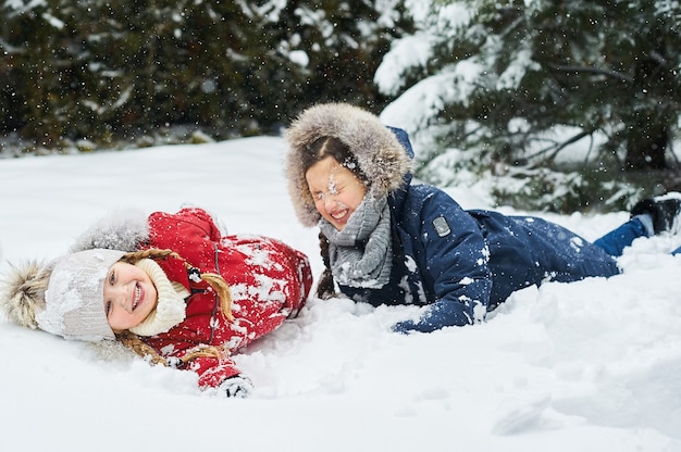 Crianças fofas brincando na neve ao ar livre perto das árvores de natal