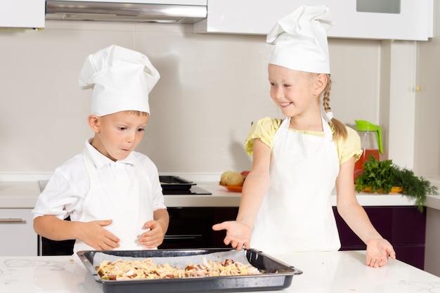 Crianças fofas fazem uma deliciosa pizza na mesa branca