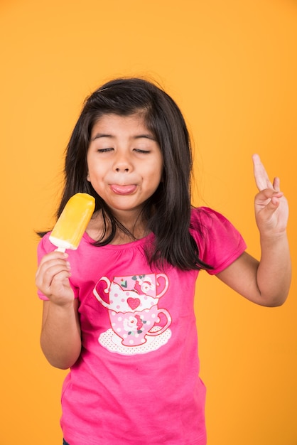 Crianças fofas indianas ou asiáticas comendo sorvete ou barra de manga ou doce. Isolado sobre fundo colorido