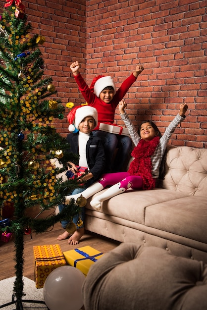 Crianças indianas asiáticas fofas celebrando o Natal em casa com o chapéu do Papai Noel, presentes e árvore de Natal