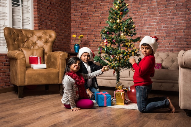 Crianças indianas asiáticas fofas celebrando o Natal em casa com o chapéu do Papai Noel, presentes e árvore de Natal