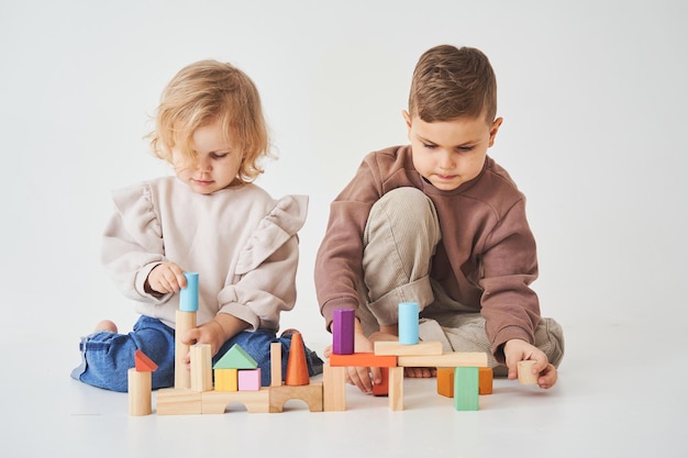 Crianças irmão e irmã sorrindo se divertindo e brincando de brinquedo de tijolos coloridos no fundo branco As crianças sorriem e se divertem juntos