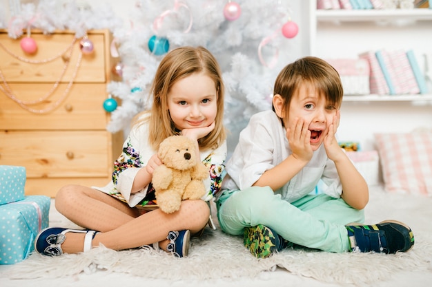 Crianças lindas e engraçadas, posando para a câmera em uma sala com decorações de festas de ano novo.