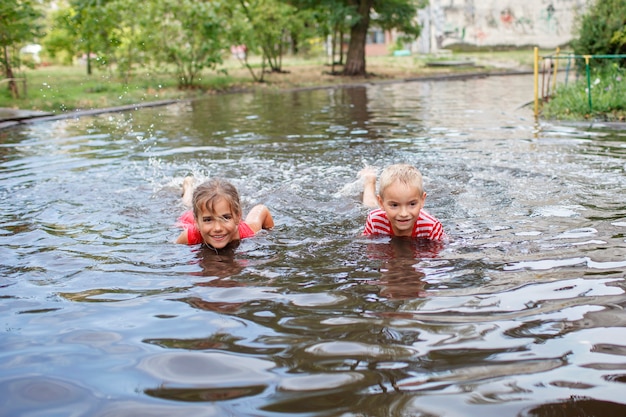 Crianças lindas pulando e nadando nas poças após a chuva quente de verão, infância feliz