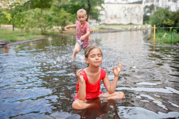 Crianças lindas pulando e nadando nas poças após a chuva quente de verão, infância feliz