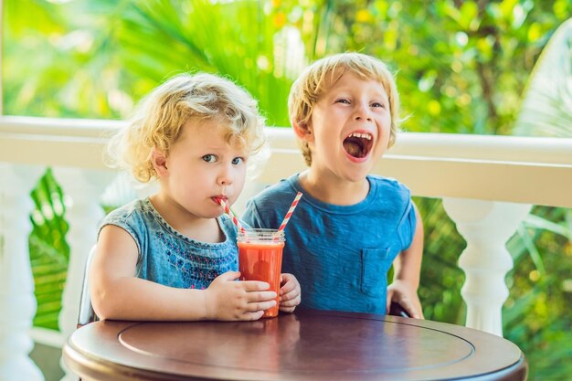 Crianças, menino e menina, bebem suco de laranja de mamão