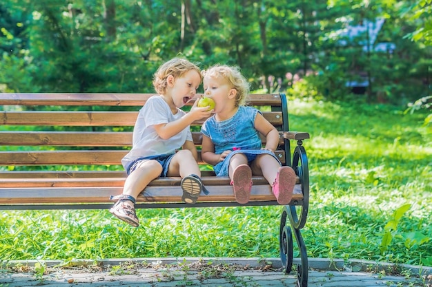 Crianças, menino e menina, sentados em um banco à beira-mar comendo uma maçã