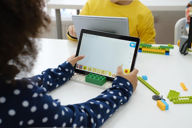 Crianças multiétnicas no robô de codificação de aula de tecnologia no tablet