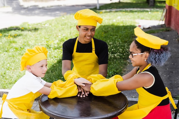 Crianças multirraciais cozinham tocando as mãos juntas formando pilha Amizade de crianças multinacionais Cozinheiros de infância com chapéu de chef e uniforme de avental amarelo colocam as mãos umas nas outras