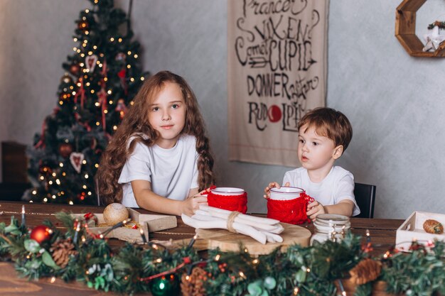 Crianças na decoração de Natal com chá em casa aconchegante com luzes coloridas do ano novo